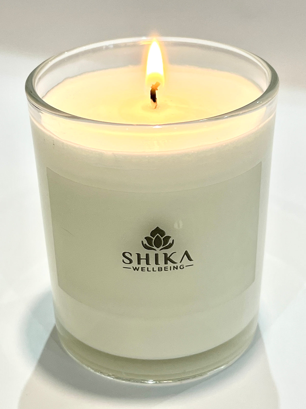 Candle in a glass jar with 'Shika Wellbeing' logo on a light background