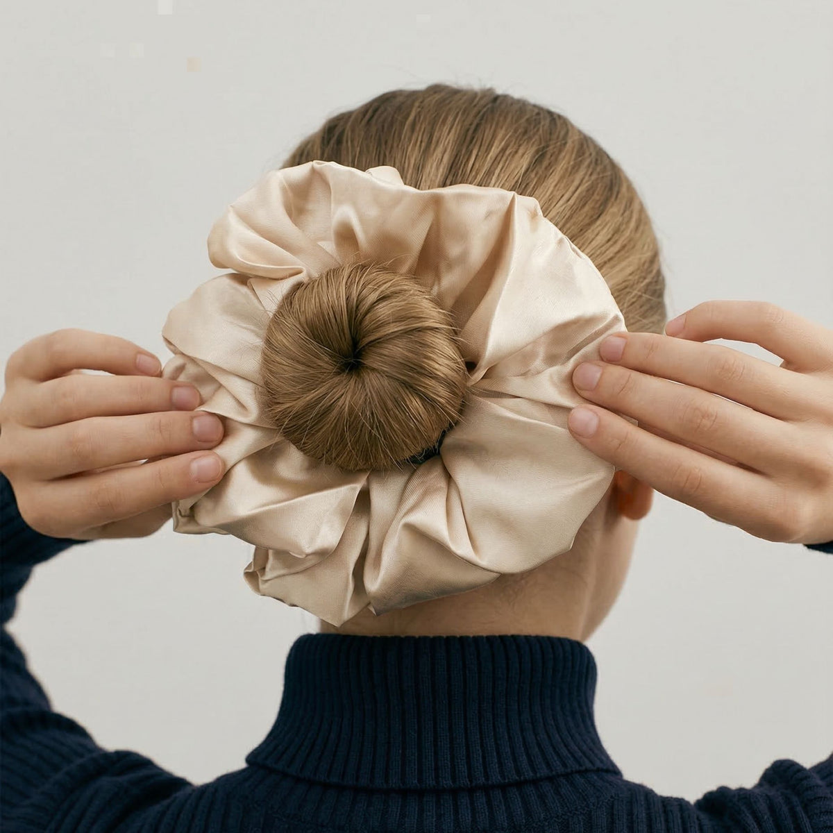 Person holding a beige scrunchie with hair on a plain background