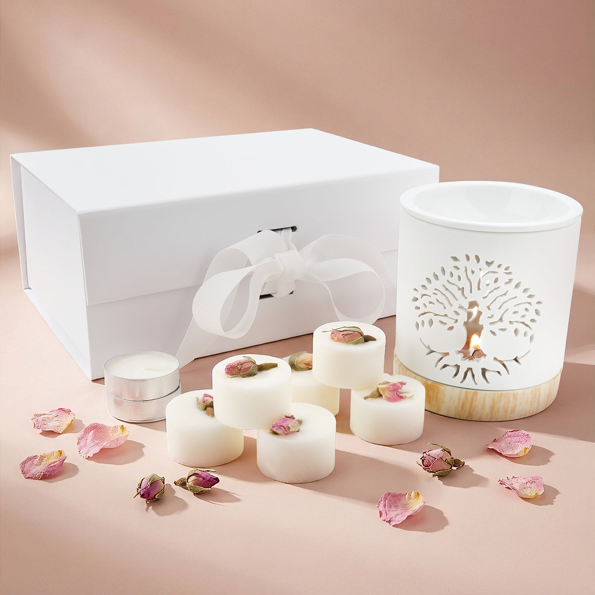 Set of white candles with decorative elements on a pink surface, featuring a white box with a bow.