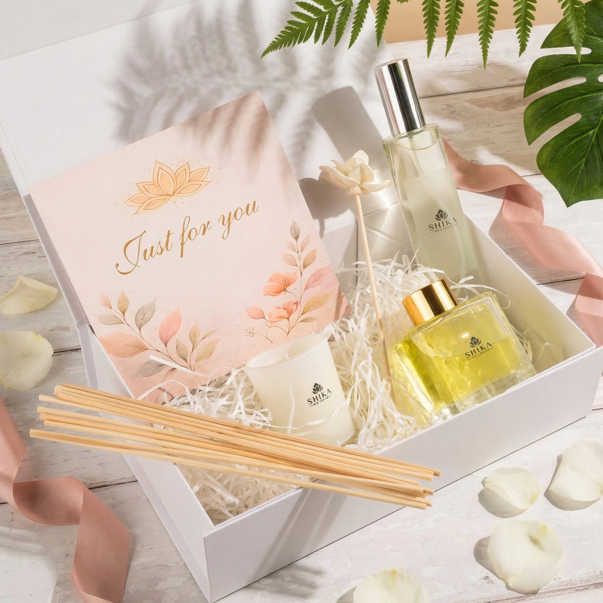Gift set with two bottles, a candle, and reed diffusers in a decorative box on a wooden surface.