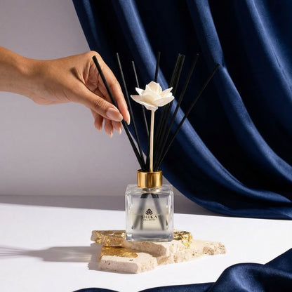 Hand holding a diffuser with a white flower on top against a blue curtain background