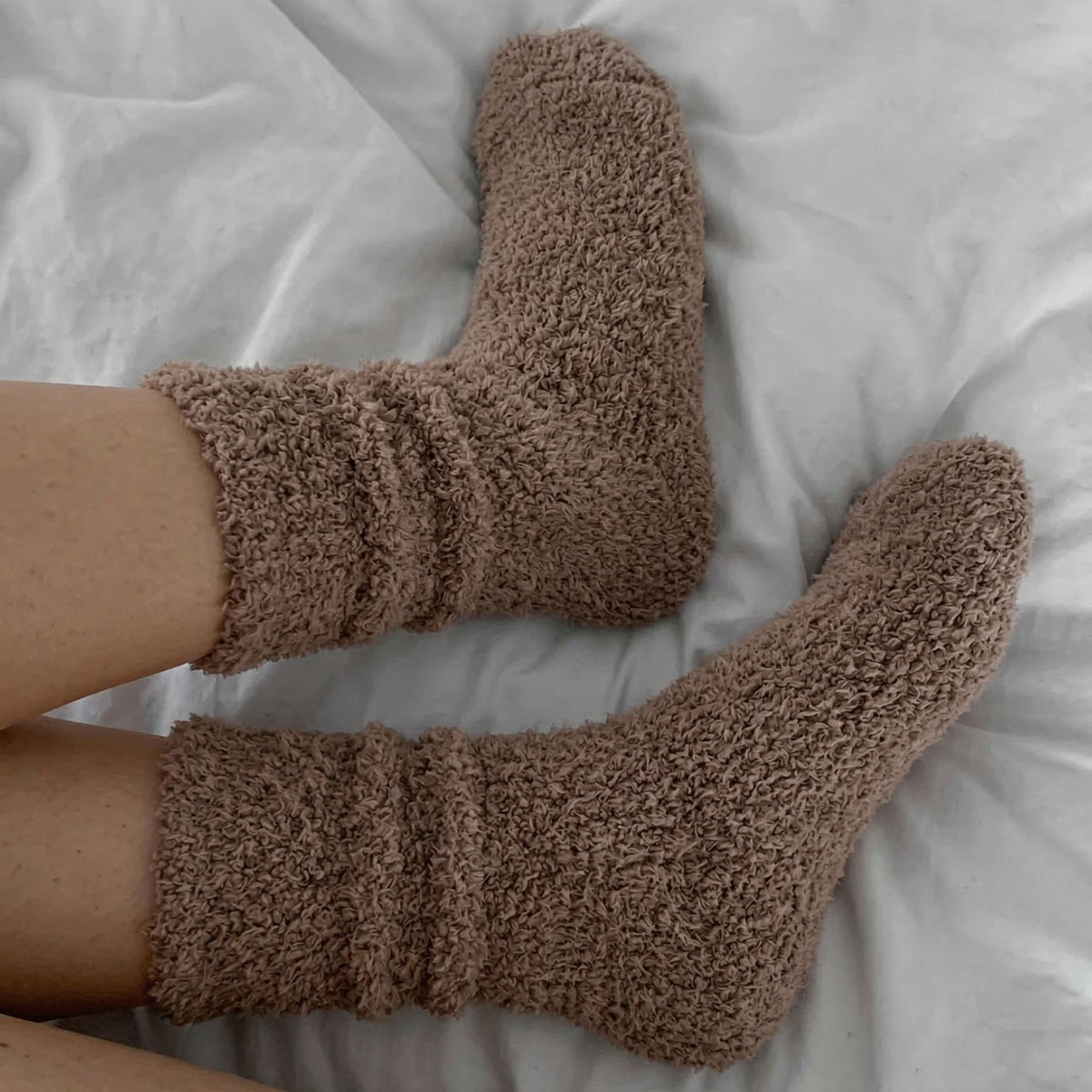 Brown fuzzy socks on a white bed