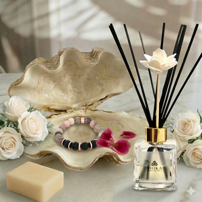 Decorative setting with an open shell, flowers, a bracelet, soap, and a diffuser on a light surface.