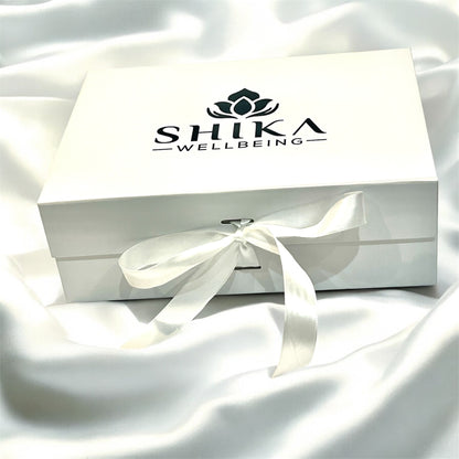 White gift box with a bow and Shika Wellbeing logo on a white fabric background