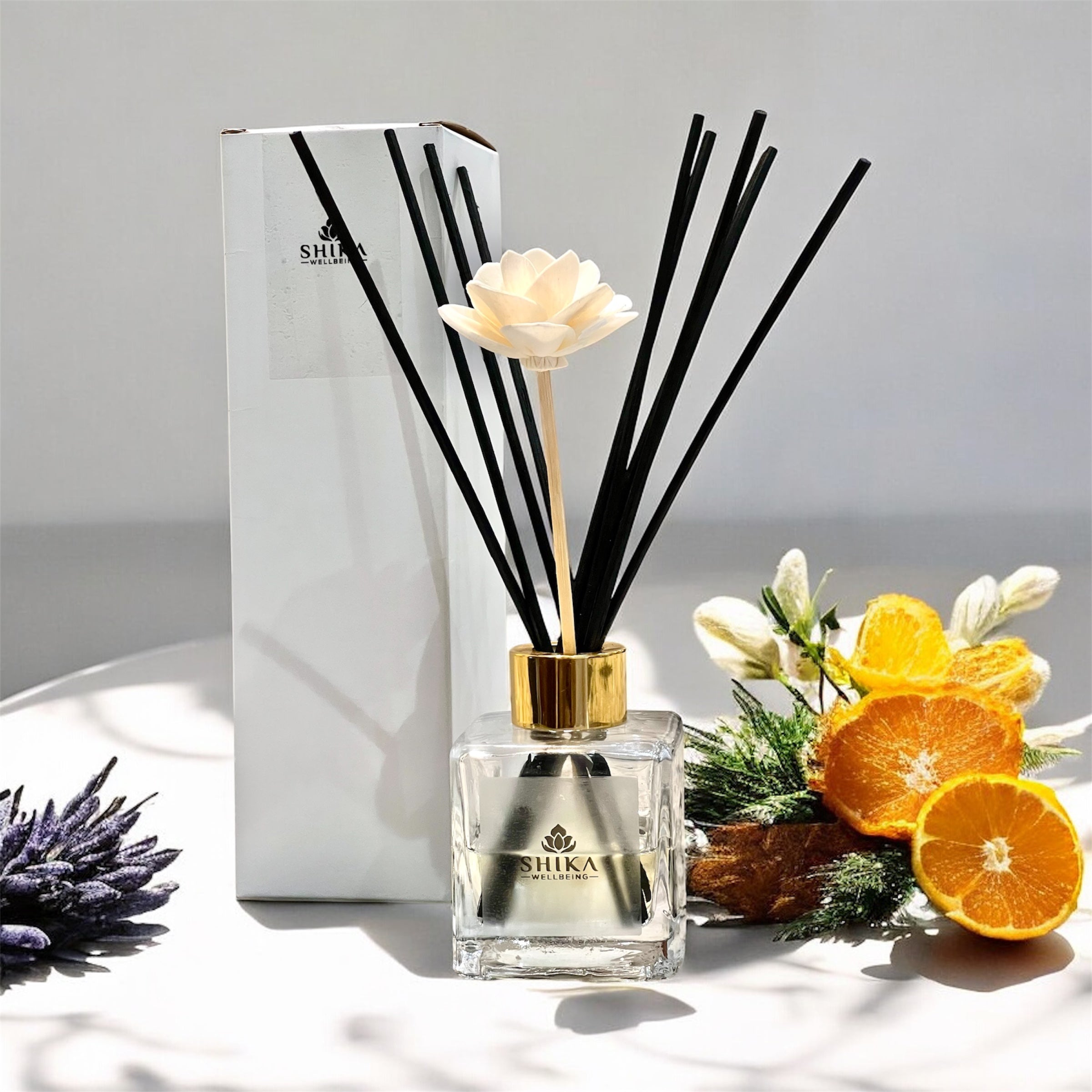 Shika diffuser with black reeds, white flower, and oranges on a light surface