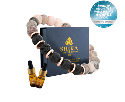 Bracelet with black and beige beads and two bottles of Shika Wellbeing oil on a white background.