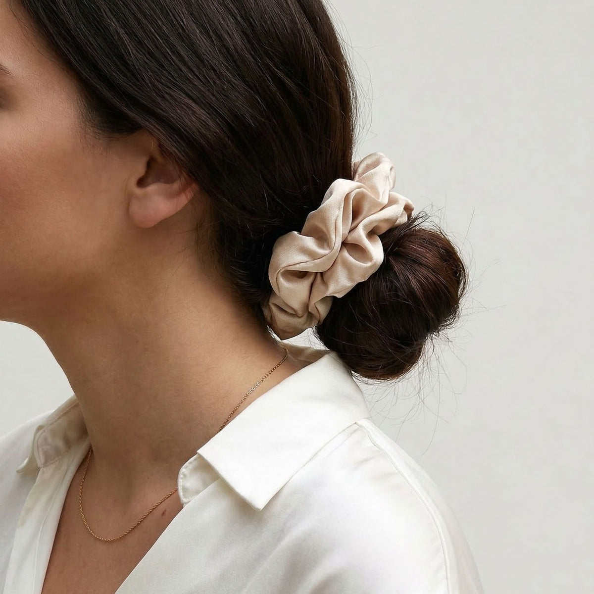Woman with a beige scrunchie in her hair against a plain background