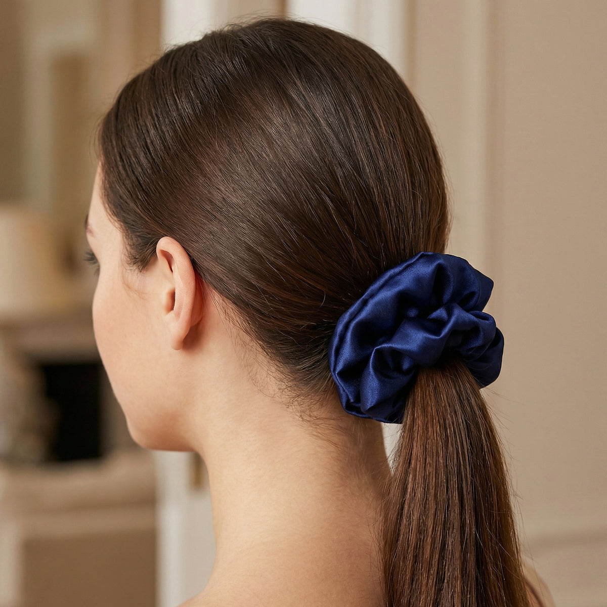 Woman with a blue scrunchie in her ponytail against a neutral background