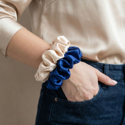 Person wearing two scrunchies, one beige and one blue, on a neutral background.